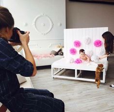 a woman taking a photo of a baby in a crib with pink pom - poms