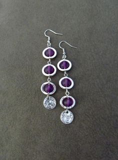 two pairs of purple and silver earrings on a black surface, with one pair dangling from the