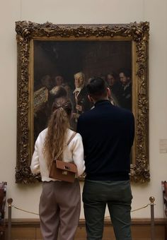 a man and woman looking at a painting in an art museum with people standing around