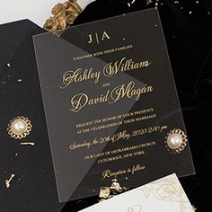 an elegant black and gold wedding card with white flowers on the table next to it