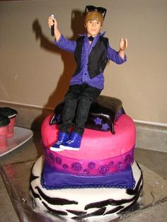 a cake with a doll sitting on top of it and holding a remote control in one hand