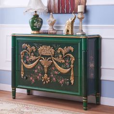 a green cabinet with gold decorations on it in front of a blue and white wall