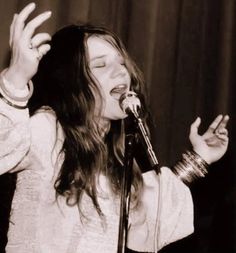 a woman singing into a microphone with her hands in the air