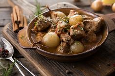 a bowl filled with meat and potatoes on top of a wooden tray next to spoons