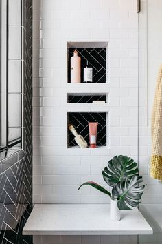 a white tiled bathroom with black and white tiles on the walls, shelves holding personal care items