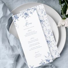 a table setting with a menu card and flowers on the placemat, next to a napkin