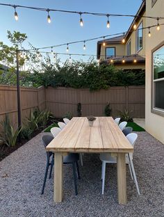 a wooden table sitting in the middle of a gravel covered yard with lights strung above it