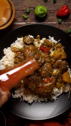 someone is dipping sauce on top of some rice in a black bowl with green peppers