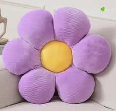 a purple flower shaped pillow sitting on top of a white couch next to a statue