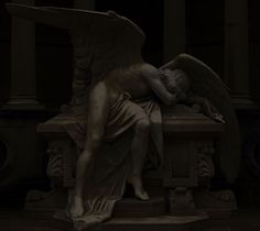 an angel statue laying on top of a bench in a dark room next to columns