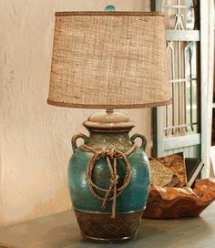 a lamp that is sitting on top of a table next to a vase with a rope wrapped around it