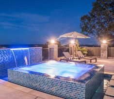 an outdoor hot tub lit up at night with lights on the side and umbrella over it