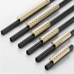 six black and gold colored chopsticks on a white surface