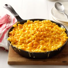 a skillet filled with macaroni and cheese on top of a wooden cutting board