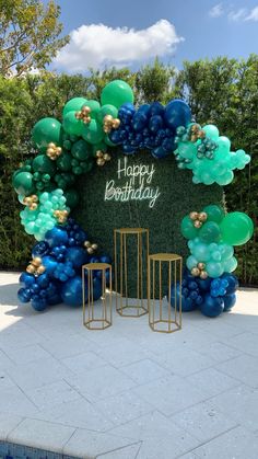 a happy birthday balloon arch with blue, green and gold balloons in front of a swimming pool