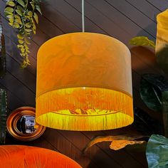 a yellow lamp hanging from a ceiling next to plants