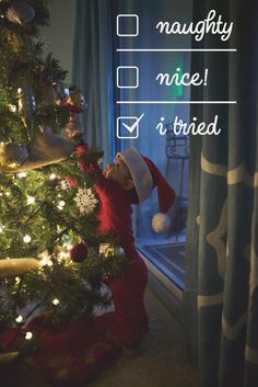 a little boy standing in front of a christmas tree with his hands on the top of it