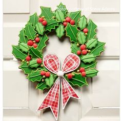 a christmas wreath decorated with holly leaves and red berries hangs on the front door of a house