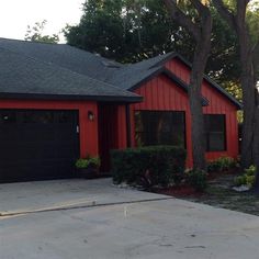 a red house with black garage doors and trees