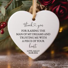 a white heart ornament hanging from a christmas tree with red flowers and greenery