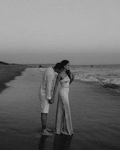 a man and woman standing on top of a beach next to the ocean