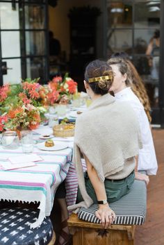 two women sitting at a table with flowers in vases and plates on the table