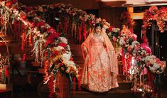 a woman in a wedding dress standing on stairs with flowers and garlands around her