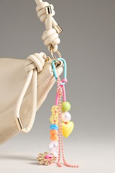 a white purse with several colorful beads hanging from it's handle and a keychain attached to the strap