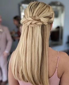 a woman with long blonde hair wearing a half - up braid and pink dress in front of a mirror