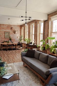 a living room filled with lots of furniture and plants on top of a hard wood floor