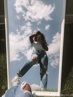 a woman taking a selfie in front of a mirror with grass and clouds behind her