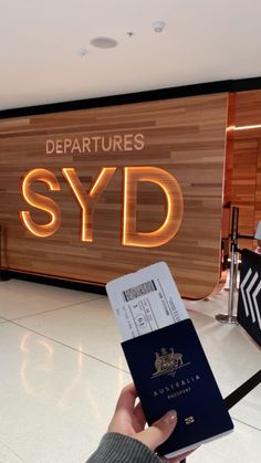 someone is holding their passport in front of the departure sign at sydney airport, australia