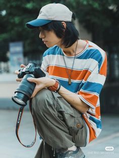 a man sitting on the ground with a camera in his hand and wearing a hat