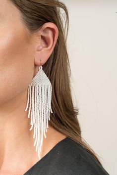 These earrings feature a beautiful curtain of white beads, adding a unique visual texture and charm. It has been thoughtfully designed and handcrafted in our hometown of Boulder, Colorado. White Beaded Fringe Dangle Earrings, White Beaded Fringe Dangle Jewelry, White Beaded Fringe Long Drop Earrings, White Beaded Long Drop Earrings, White Long Drop Chandelier Earrings With Dangling Beads, White Long Drop Beaded Fringe Earrings, White Long Drop Jewelry With Beaded Fringe, White Beaded Fringe Earrings As Gift, White Beaded Fringe Earrings For Gift