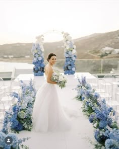 a woman in a wedding dress is standing under an arch with blue and white flowers