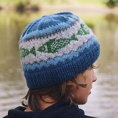 a young boy wearing a blue and white knitted hat looking out over the water