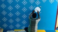 a man painting a wall with blue and white snowflakes on the wall behind him