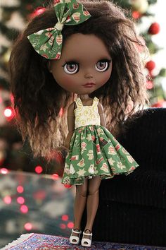 a close up of a doll on a table near a christmas tree with lights in the background