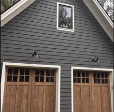 two brown garage doors in front of a gray house with white trim on the windows