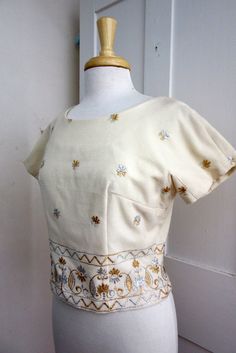 "White Wool with Gold and Silver Embroidery 5 covered button in back Lined Size Bust - 38\" Waist - 32\" Arm from Neck - 8.5\" Length - 18\" Condition - Excellent" Fitted Embroidered Beige Top, Elegant Fitted Cotton Embroidered Top, Fitted Cream Top With Buttons, Fitted Cream Blouse With Floral Embroidery, Fitted Cream Tops With Floral Embroidery, Fitted Vintage Embroidered Top With Short Sleeves, Fitted Vintage Embroidered Short Sleeve Top, Cream Fitted Cotton Blouse, Fitted Cream Cotton Blouse