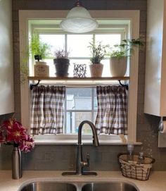 a kitchen sink sitting under a window with potted plants on top of the windowsill