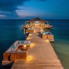 a dock with lounge chairs and lights on it at night time, overlooking the ocean