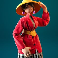 a doll wearing a red coat and yellow hat with her hands on her head,