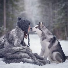 a woman sitting in the snow with a husky dog next to her, both looking at each other