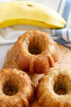 three donuts on a wooden cutting board with a banana in the backround