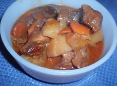 a white bowl filled with meat and vegetables on top of a blue table cloth,