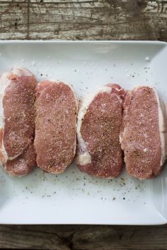 four raw meats on a white plate with seasoning sprinkled around them