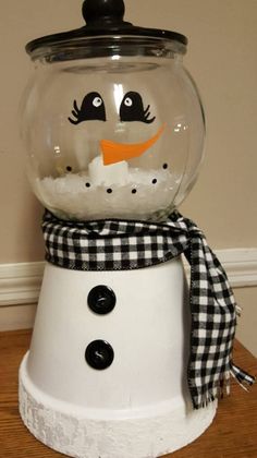 a snowman made out of a glass bowl on top of a wooden table with a black and white checkered scarf