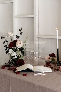 an open book sitting on top of a table next to a vase with flowers in it