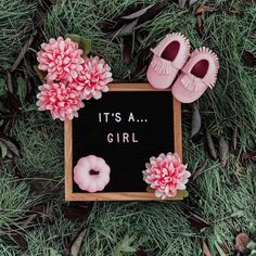 it's a girl sign with pink flowers and baby shoes on the grass next to it